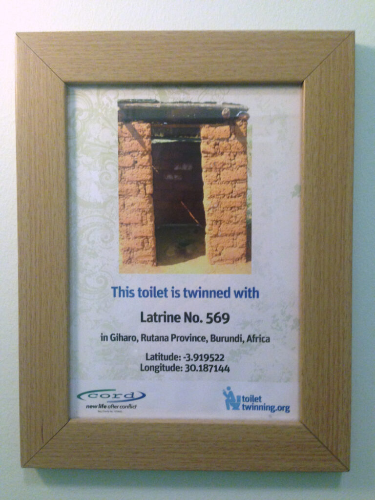 a sign saying 'this toilet is twinned with Latrine No 569' giving the country, latitude and longitude.